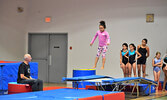 Gymnasts soared through the air on the trampoline as Coach Mike Lang (far left) looks on. - Jesse Bonello / Bulletin Photo